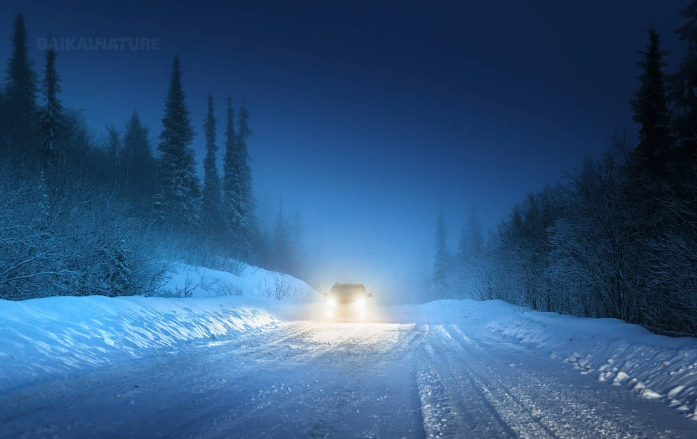 Автомобильные фары на машине двигающийся по дороге через зимний лес в России.