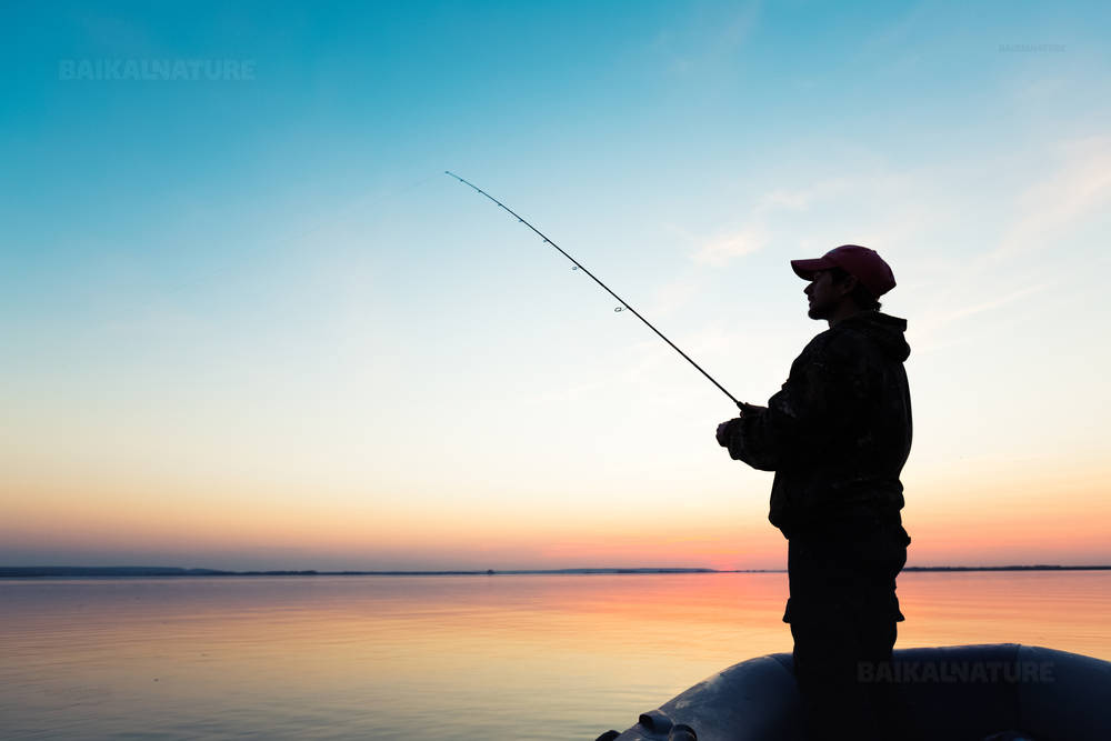 Человек рыбачующий с лодки на закате солнца.